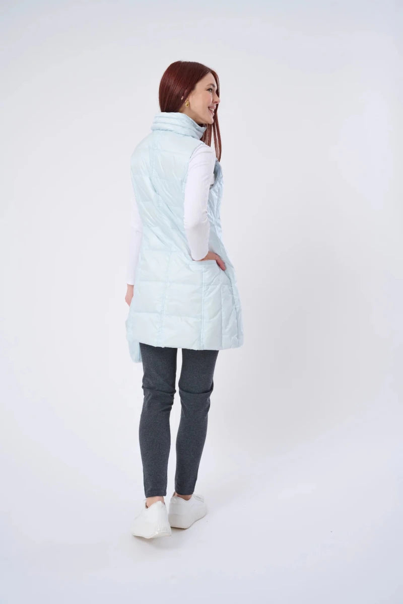 Woman wearing a light blue puffer vest over a white shirt with gray pants on a white background