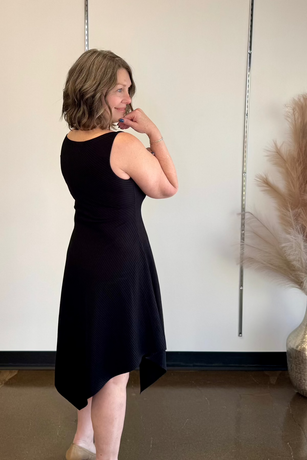 Woman wearing a black dress standing sideways looking in the distance.