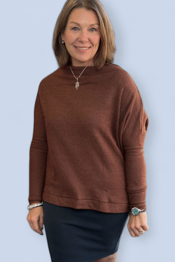 Woman wearing a brown sweater and black skirt against a light blue background