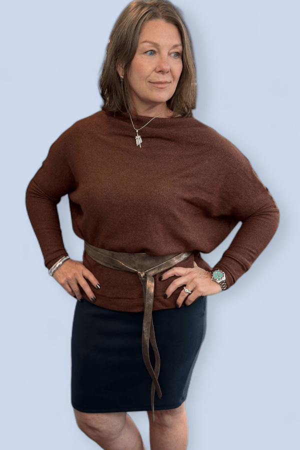 Woman wearing a brown sweater and black skirt against a light blue background