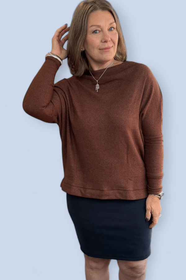 Woman wearing a brown sweater and black skirt against a light blue background