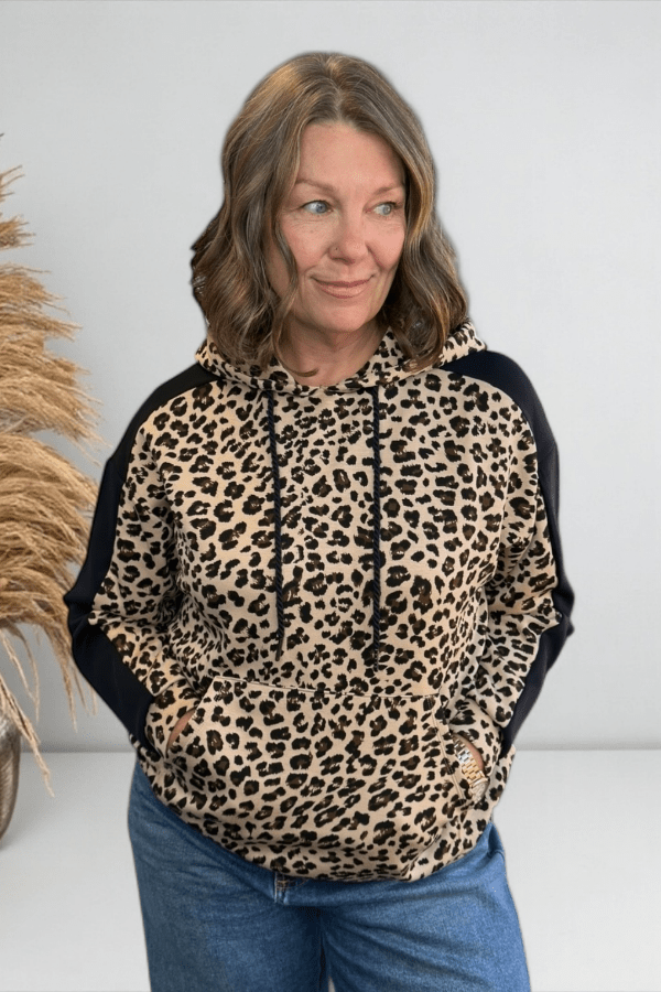 Woman wearing a leopard print hoodie with black sleeves against a white background