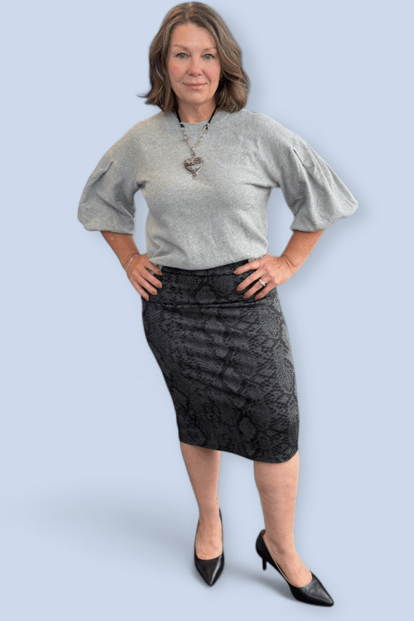Woman wearing a gray top and black patterned skirt against a light blue background
