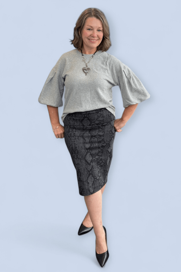 Woman wearing a gray top and black patterned skirt on a light blue background