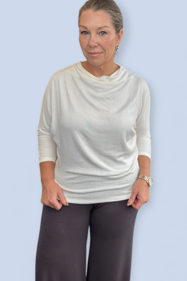 Woman wearing an ivory top standing in front of a pale blue backdrop.