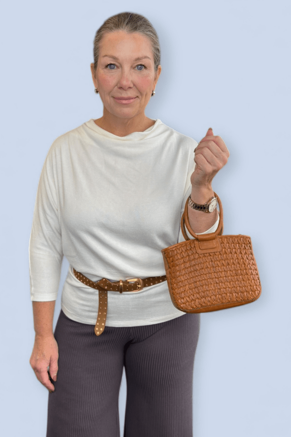 Woman wearing an ivory 3/4 sleeve top belted and holding a small purse.