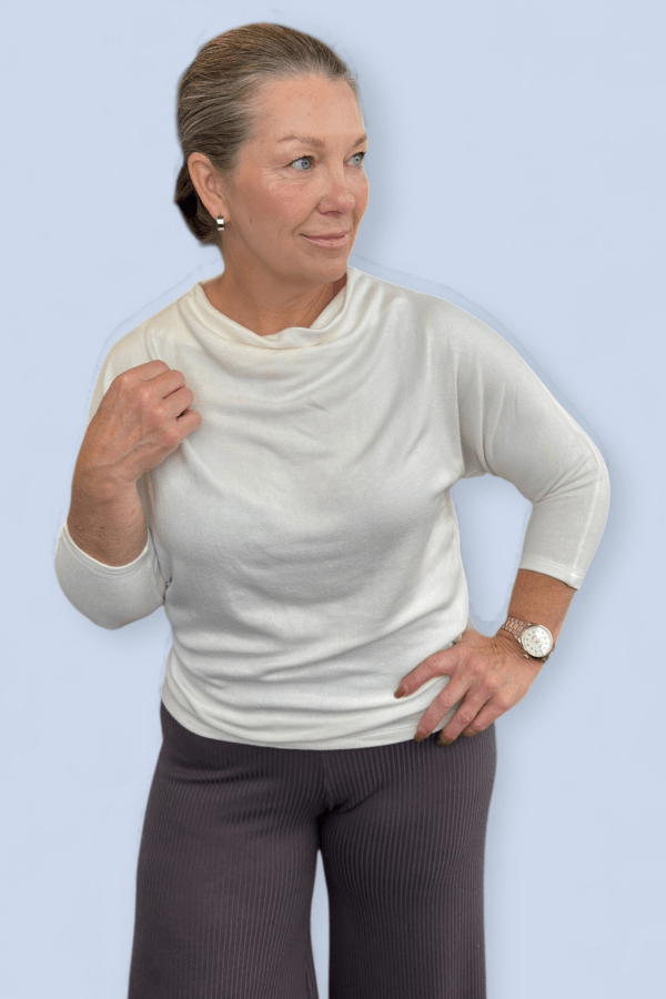 Woman wearing an ivory top with hand on hip and looking away.