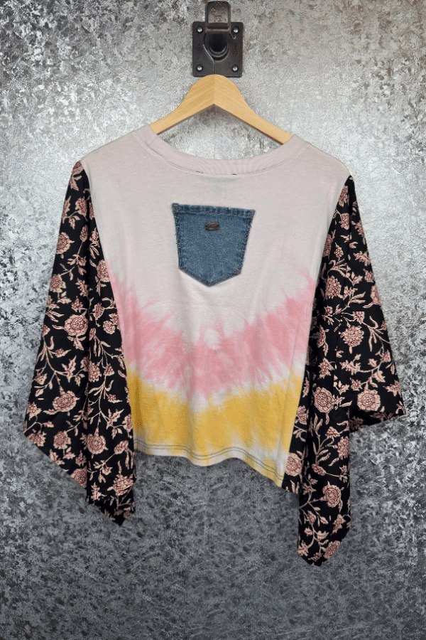 Floral-patterned shirt with tie-dye design on a hanger against a textured wall.