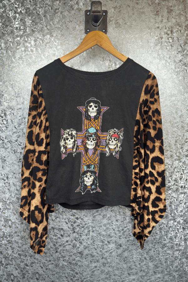Black long-sleeve shirt with leopard print sleeves and graphic design on a hanger against a textured gray background.