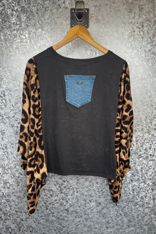 Black long-sleeve shirt with leopard print sleeves and blue pocket on a hanger against a textured gray background