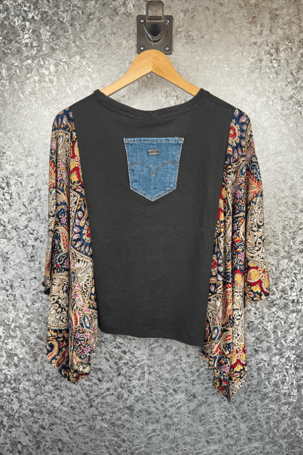 Black t-shirt with a blue pocket design, worn over a colorful patterned top, on a textured gray background.