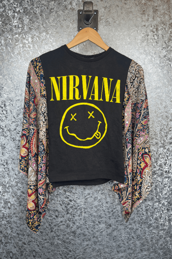 Black shirt with Nirvana logo and smiley face design on a hanger against a textured wall.