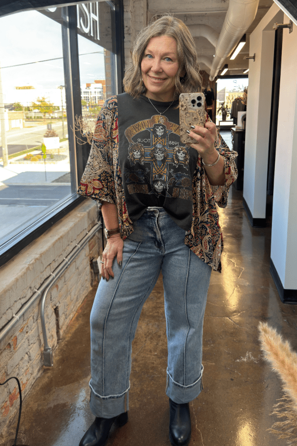 Woman taking a mirror selfie in a casual outfit with a patterned cardigan, graphic t-shirt, and jeans.