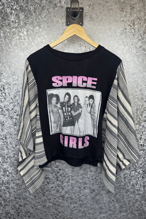Black t-shirt with Spice Girls graphic on a hanger against a textured wall.
