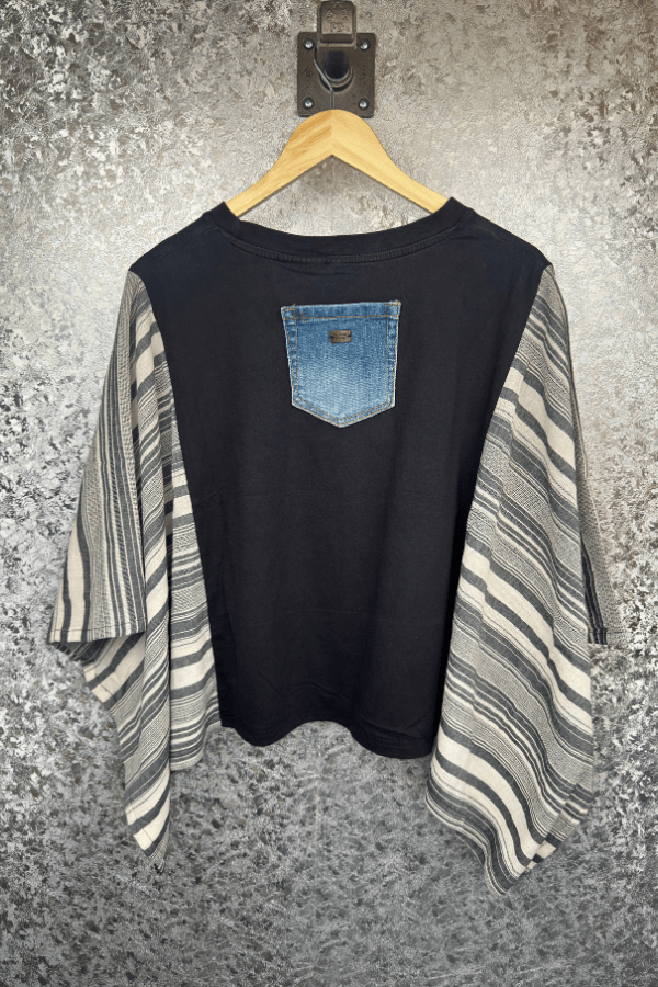 Black long-sleeve shirt with denim pocket design on a hanger against a textured wall.