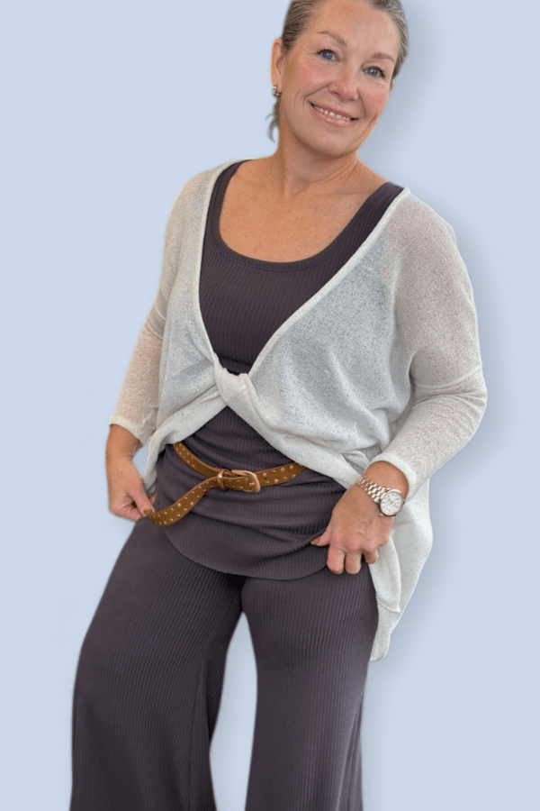 Model wearing a gray pant set and ivory twist top with a studded belt.
