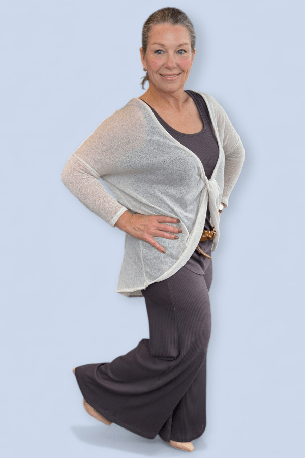 Woman wearing a beige cardigan over a dark top and brown pants on a light blue background