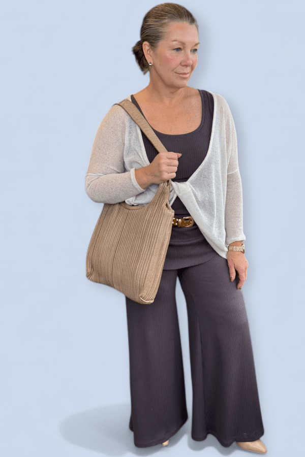 Woman wearing a matching top and wide leg pant with an ivory sweater and large taupe purse.