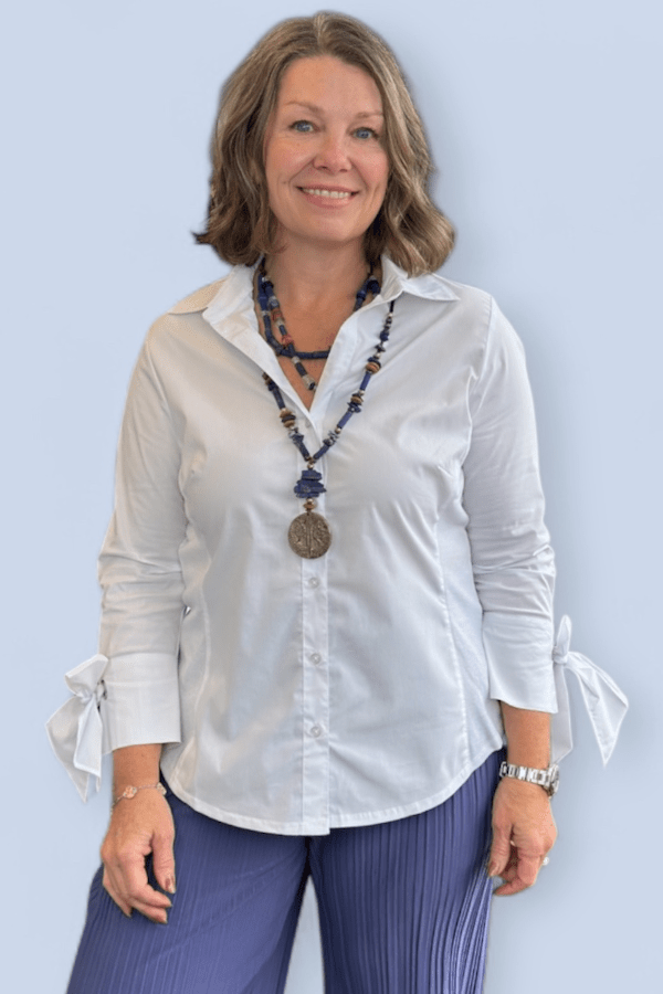 Woman wearing a white blouse with ruffled sleeves against a light blue background