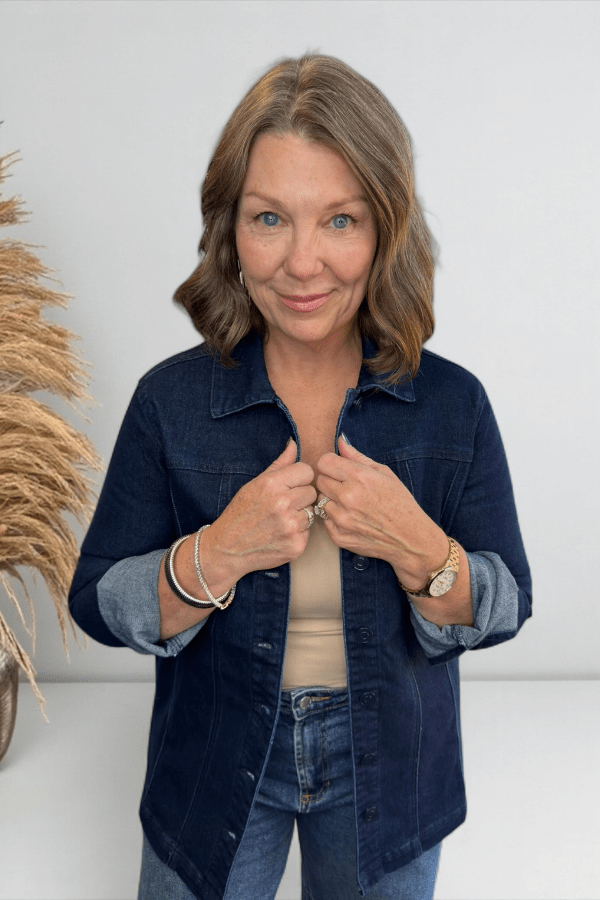 Woman wearing a navy denim jacket with rolled-up sleeves, standing against a white wall.
