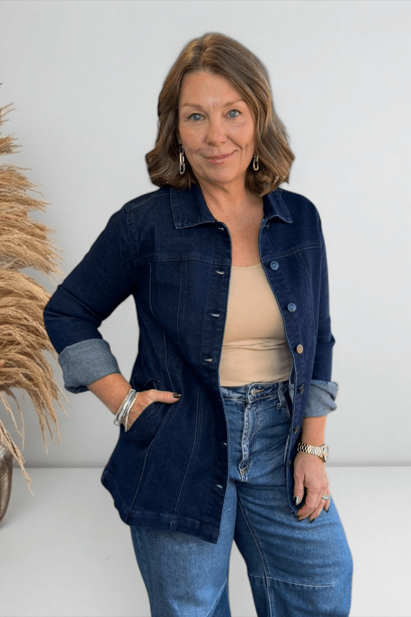 Woman wearing a denim jacket and jeans standing against a white wall with decorative elements.