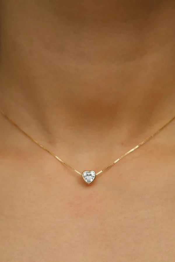 Gold necklace with a heart-shaped pendant on a person's neck
