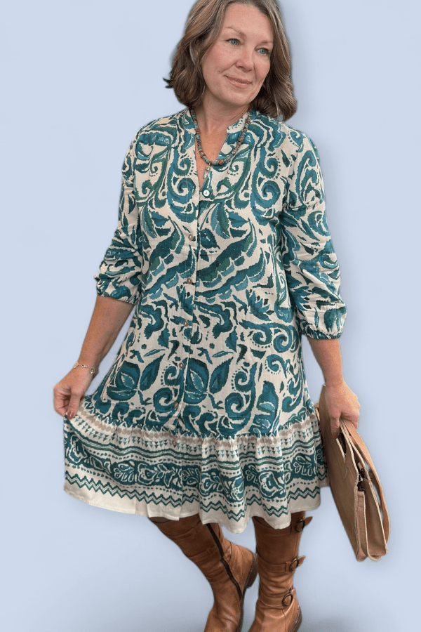 Woman wearing teal and ivory dress holding a brown purse against a light blue background.