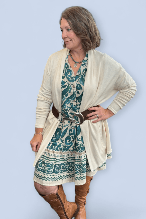 Woman wearing a blue dress with an ivory sweater belted.