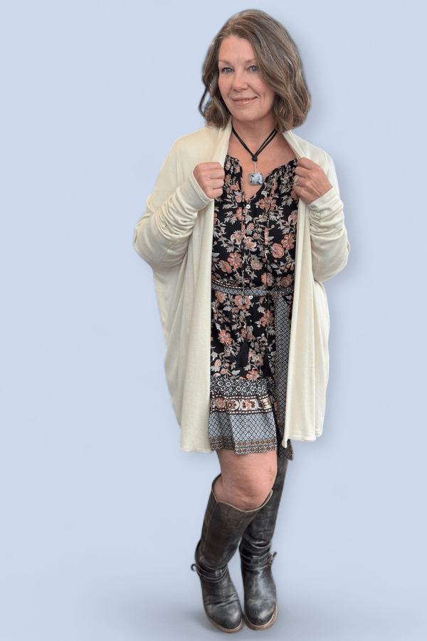 Woman wearing a floral dress with a beige cardigan and boots on a light blue background