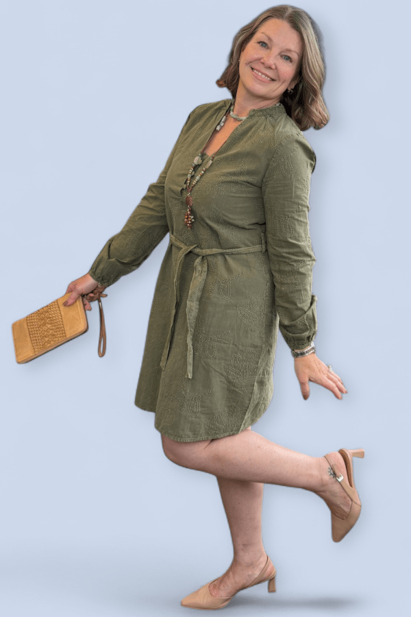 Woman wearing a green dress with a belt, holding a clutch, on a light blue background