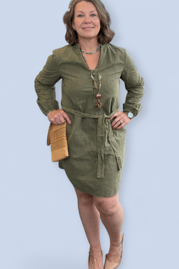 Woman wearing a green dress with a beige clutch against a light blue background