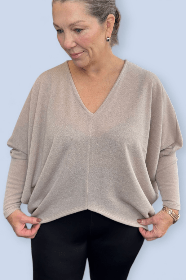 Beige ivory v neck sweater worn over a pair of black pants.