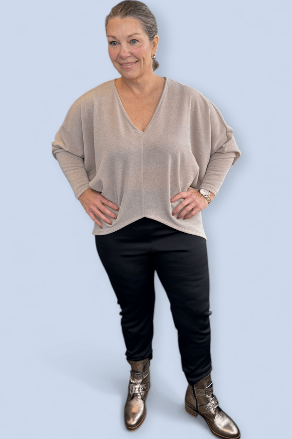 Woman wearing a beige sweater, black pants, and gold boots on a light blue background