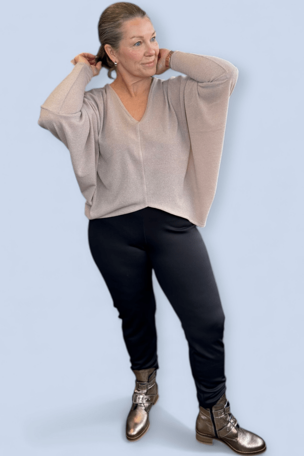 Woman wearing a gray v neck top with black pants and silver booties.