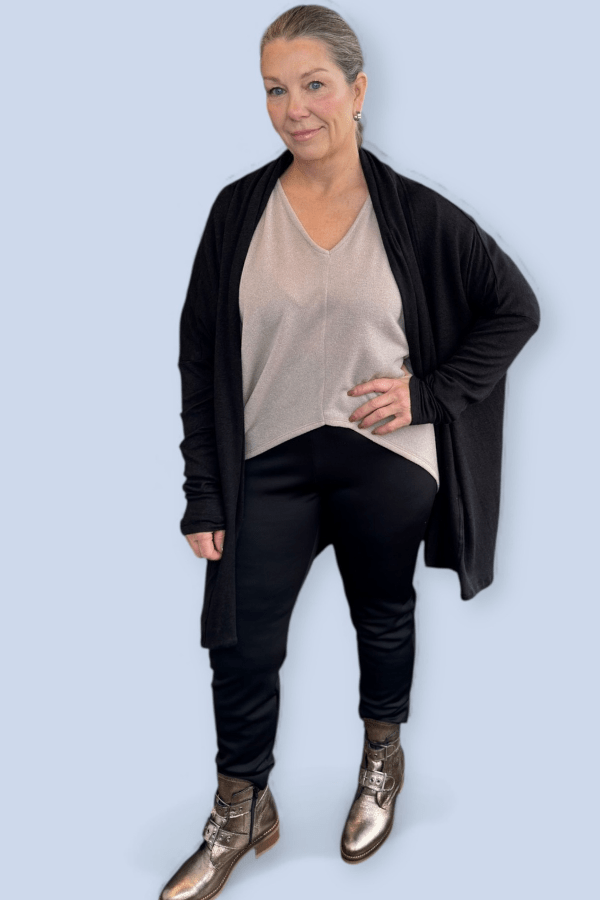 Woman wearing a black cardigan, beige top, black pants, and gold boots on a light blue background