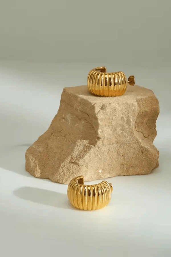 Two gold pumpkin-shaped earrings on a stone block with a neutral background