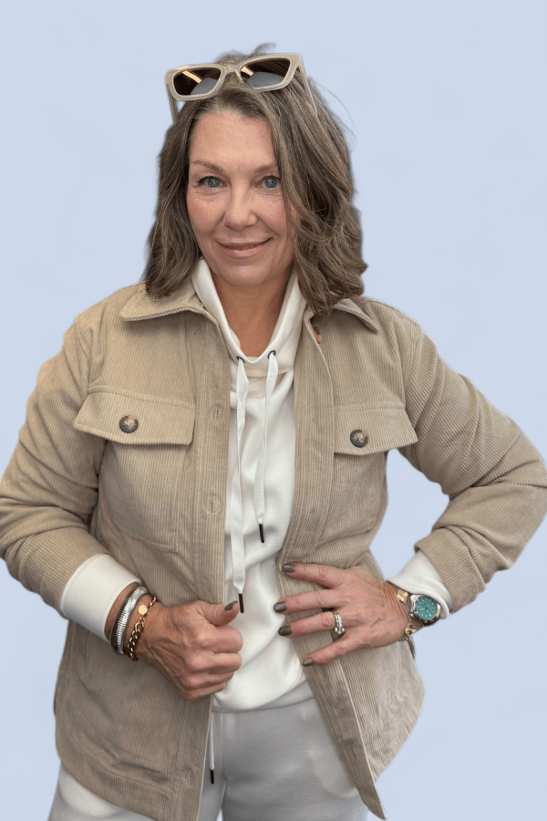 Woman wearing a beige jacket and white shirt with sunglasses on her head against a light blue background