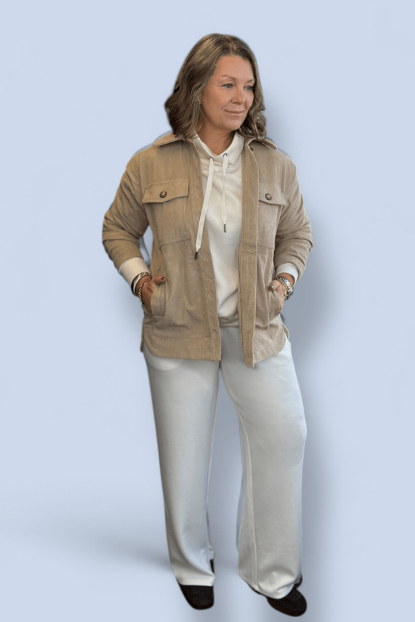 Woman wearing a beige jacket and white pants on a light blue background