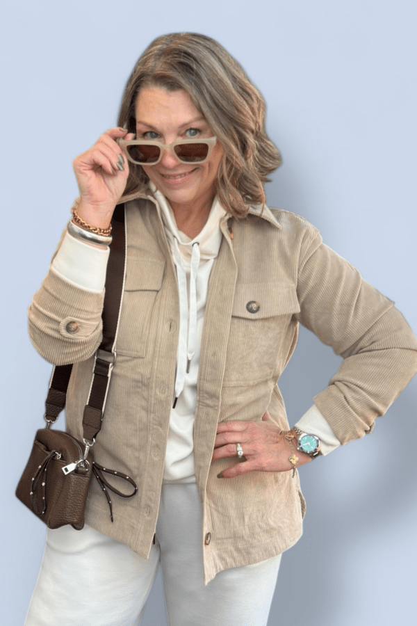 Woman wearing a beige jacket, white shirt, and sunglasses against a light blue background