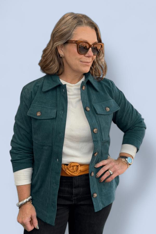 Woman wearing a green jacket over a white shirt with a yellow belt against a light blue background