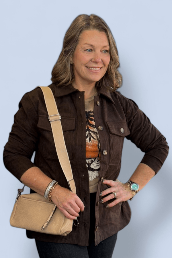 Woman wearing a brown jacket with a beige purse against a light blue background