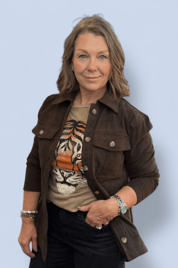 Woman wearing a brown jacket over a tiger-themed shirt against a light blue background