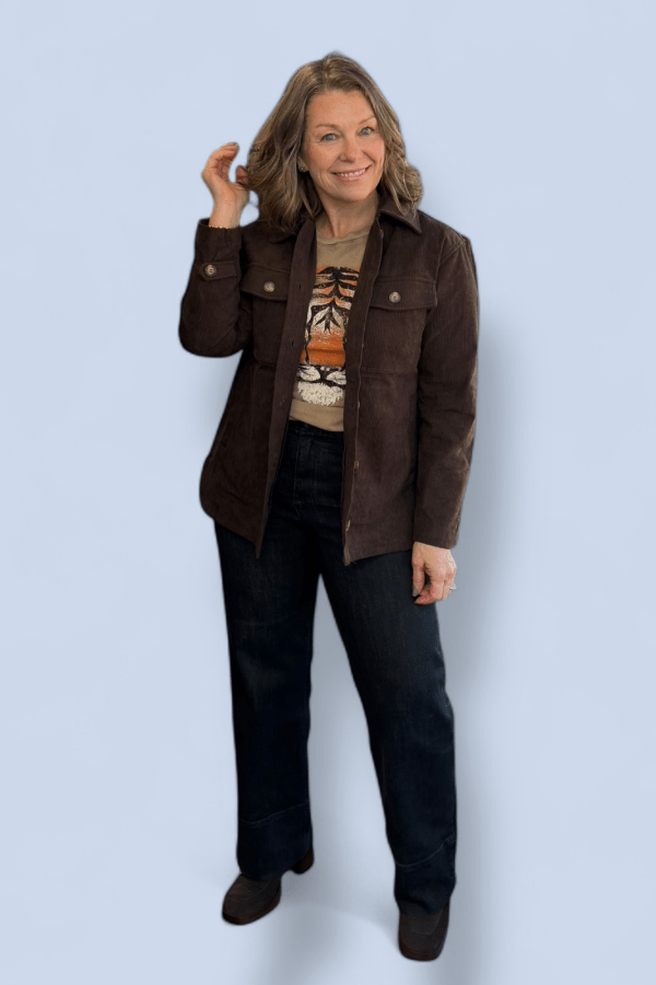 Woman wearing a brown jacket over a patterned shirt on a light blue background