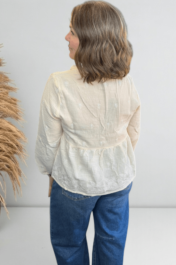 Woman wearing a cream flowy top showing the back.