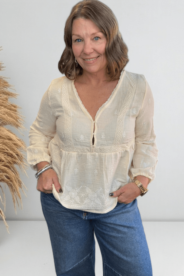 Woman wearing an ivory long sleeve v neck top with jeans.