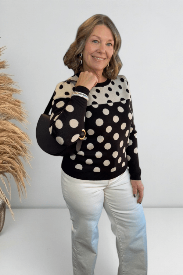 Woman wearing a black sweater with white polka dots and light blue jeans against a plain background