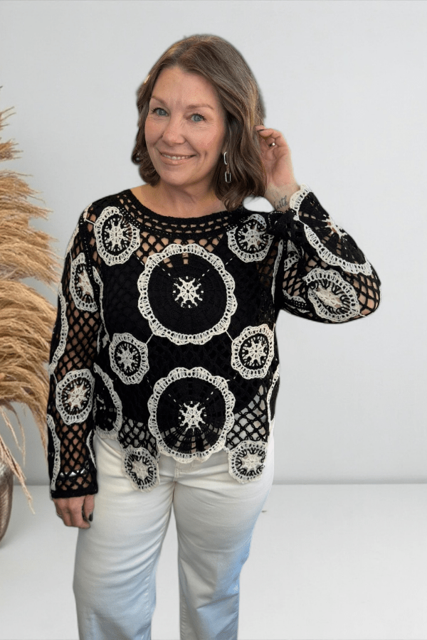 Woman wearing a black and white patterned top with white pants against a plain background