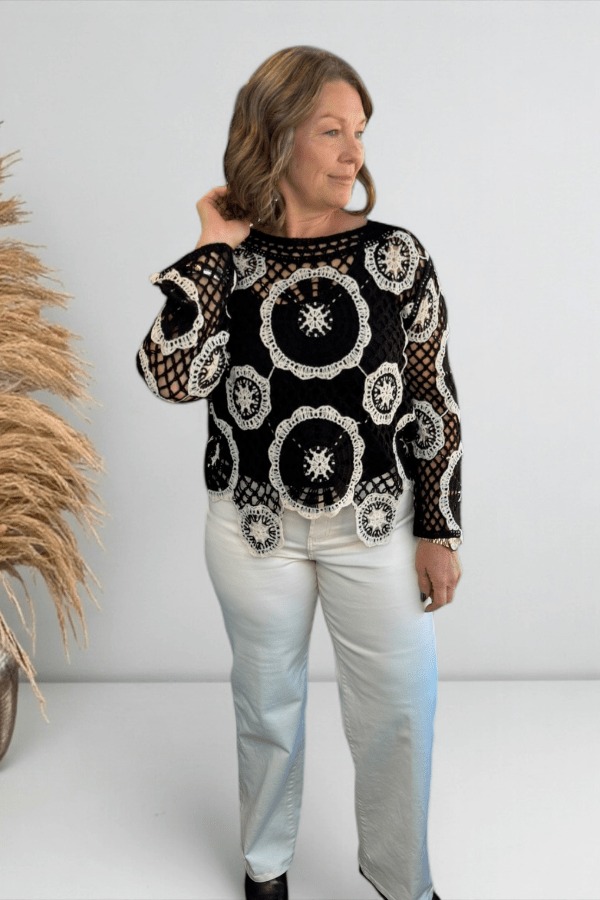 Woman wearing a black lace sweater with white patterns on a plain background