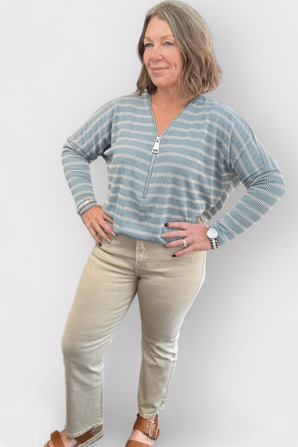 Woman wearing a striped sweater and beige pants against a white background