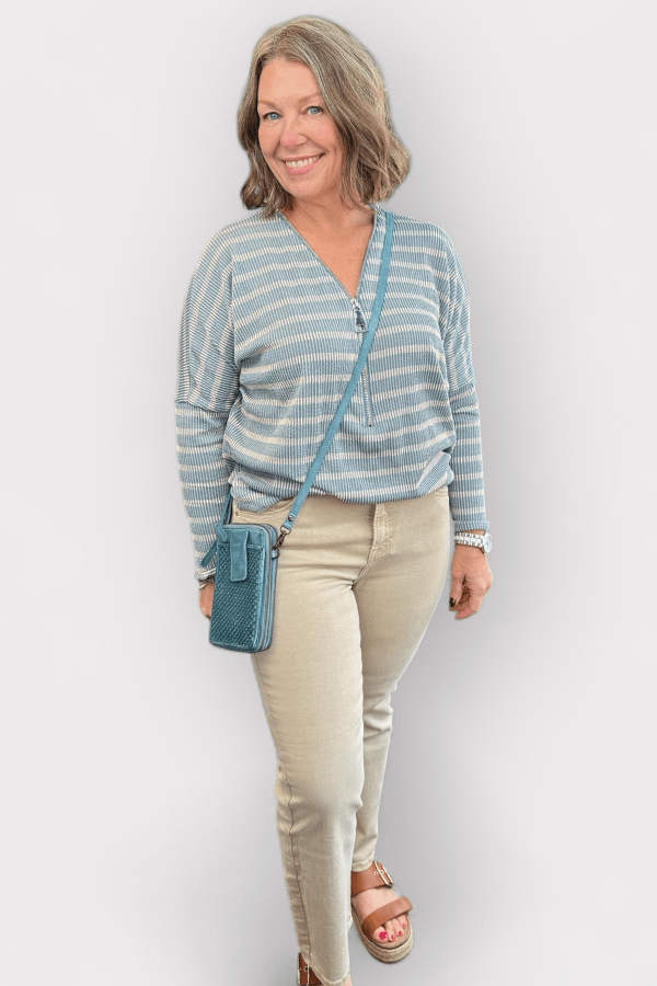 Woman wearing a striped shirt and beige pants with a blue crossbody bag against a white background